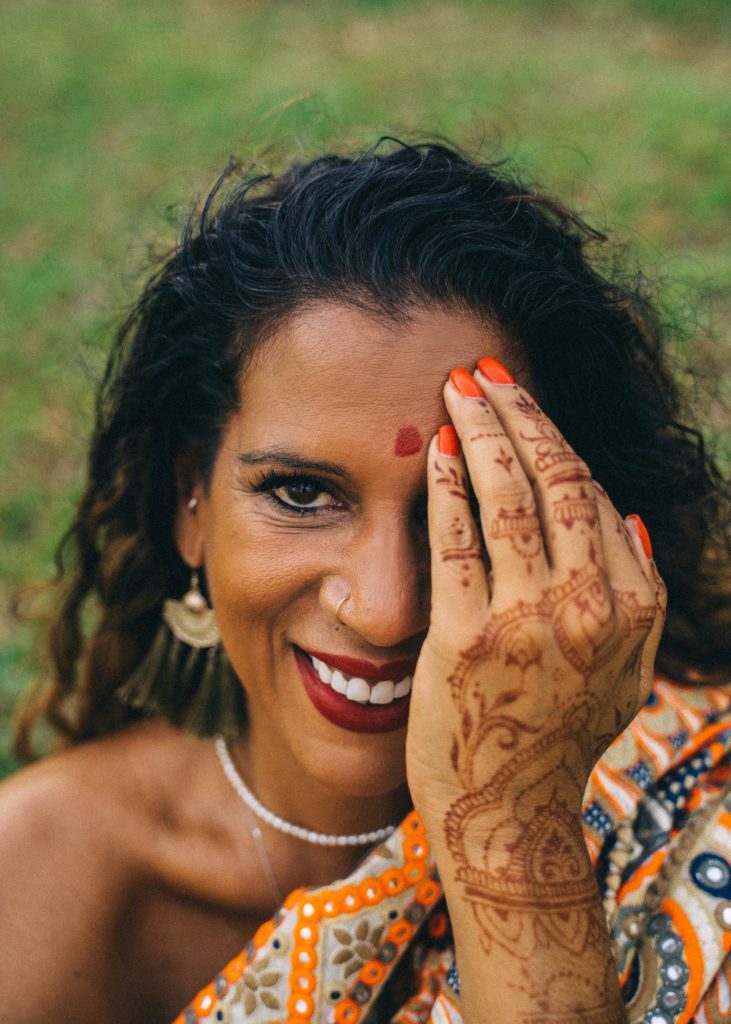 A person with henna tattoo design on one hand, covering one eye and smiling